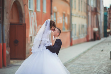 Naklejka premium Wedding photo shooting. Bride and bridegroom walking in the city. Married couple embracing and looking at each other. Holding bouquet. Outdoor, full body