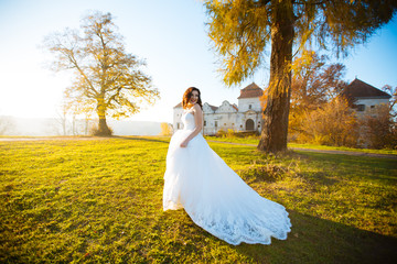 Sexy beautiful brunette bride in a white dress creates a park at sunset
