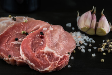 Raw pork steaks with salt, pepper and garlic on dark wooden back