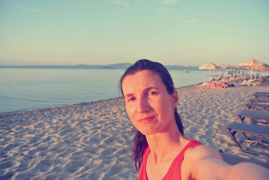 Selfie of a young woman in a red dress on the beach, on a sunny summer afternoon. Image filtered in faded, retro, Instagram style; nostalgic, vintage concept of summer travel.