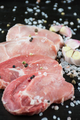 Raw pork steaks with salt, pepper and garlic on dark wooden back
