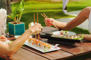 Two girls have a dinner with japanese sushi roll outdoors