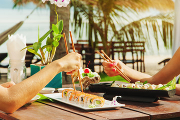 Two girls have a dinner with japanese sushi roll at the beach