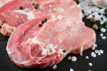 Raw pork steaks with salt, pepper and garlic on dark wooden back