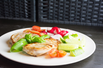 Pork steaks with vegetables on white plate on dark background