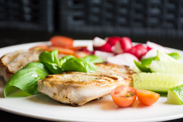 Pork steaks with vegetables on white plate on dark background