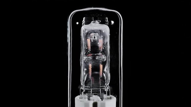 Long shaped halogen lamp blinks over black background, macro view, loop ready