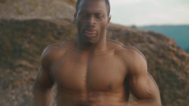 Handsome african american muscular bodybuilder with naked torso jogging outdoor. Rocky mountain landscape background