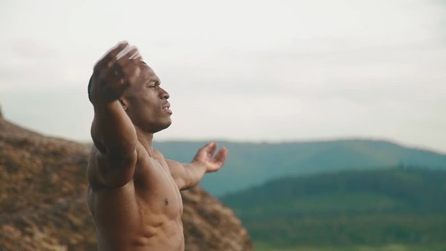 Side view of strong african american bodybuilder stretching outdoor. Mountain landscape background