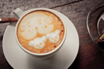 A cup of coffee with dog pattern in a white cup on wooden backgr