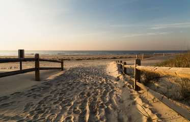 Houten leuningen aan beide zijden, als ingang van het zandstrand, voetafdrukken in het zand, golven en lucht op de achtergrond, Ocean city NJ