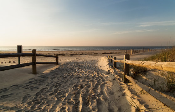 Wooden handrails on both sides, as the entrance to the sandy beach, footprints in the sand, waves and sky in the background,Ocean city NJ © Elena Milovzorova