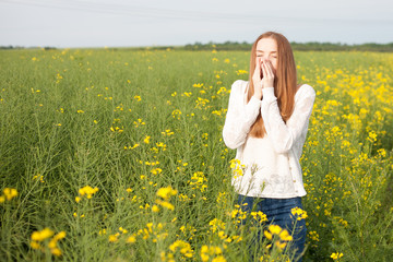 Pollen allergy, girl sneezing in a rapeseed field of flowers