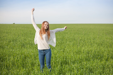 woman with open arms in the green wheat field at the morning