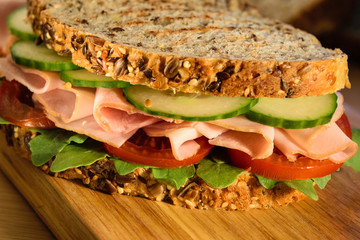Big sandwich with ham and sliced vegetables on wooden board. Close up