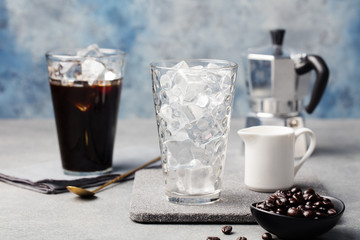 Ice coffee in a tall glass and coffee beans on a grey stone background