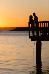 Rear view of a romantic young couple sitting on the pier enjoying stunning sunset