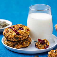 Pumpkin, oat cookies with cranberries, maple glaze and glass of milk on a blue textile background.