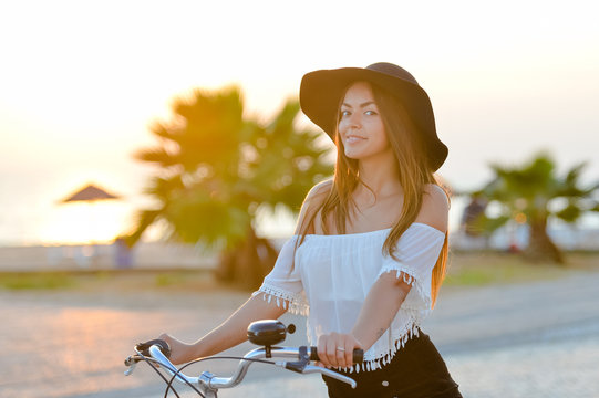 Summer sunset lifestyle image of hipster beautiful woman riding bicycle, having fun, enjoying tropical vacation 