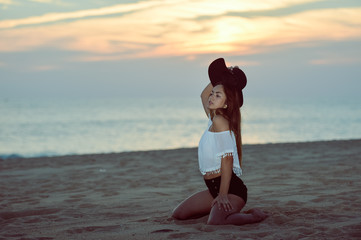 Fototapeta na wymiar Young elegant pretty lady with a hat on the beach dawn outdoors background, portrait