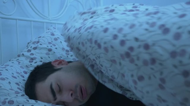 Young attractive adult alone laying in a comfortable clean bed feeling sick and caughing. He can't sleep.The scene is darker to simulate the night.
