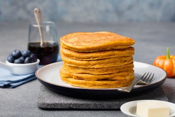 Pumpkin pancakes with maple syrup and blueberries on a plate. Grey stone background Copy space