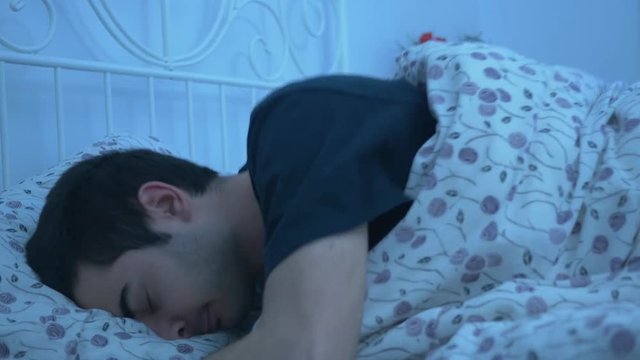 Young attractive adult alone laying in a comfortable clean bed having major problem to fall asleep by turning in different positions.The scene is darker to simulate the night.