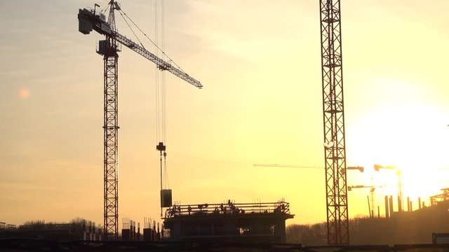 Silhouettes of crane transferring concrete plate and construction workers. 4K