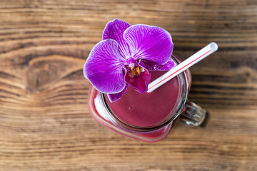 Fruit smoothie and orchid flower in glass jar, over old wooden table