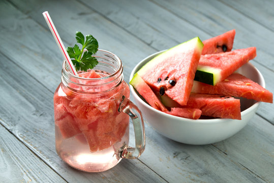 Fresh watermelon smoothie in the glass jar and bowl with watermelon slices on grey wooden background