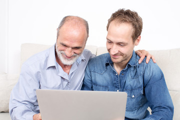 Elderly man with younger person surfing together in internet