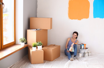 Fototapeta premium Woman choosing paint colour from swatch for new home sitting on wooden floor