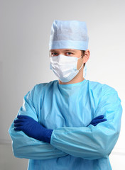 Young doctor with arms crossed, dressed in blue gown, hat and mask