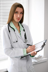 Female doctor brunette sitting  at the table near the window in hospital and typing at laptop computer