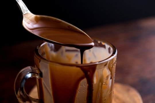 Chocolate sauce drizzling from spoon into mug