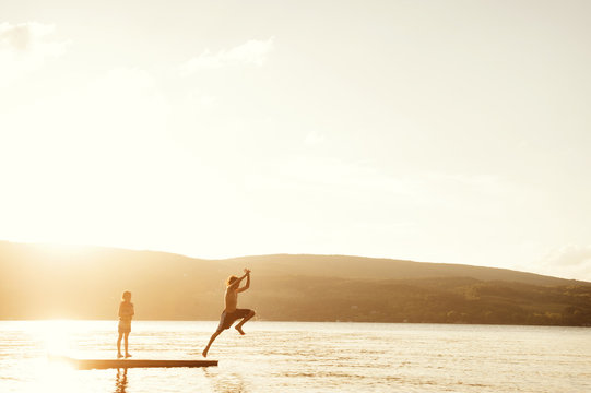 Boy Jumping Into Lake From Wooden Pier