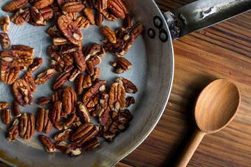 Pecan nuts in pan with wooden spoon