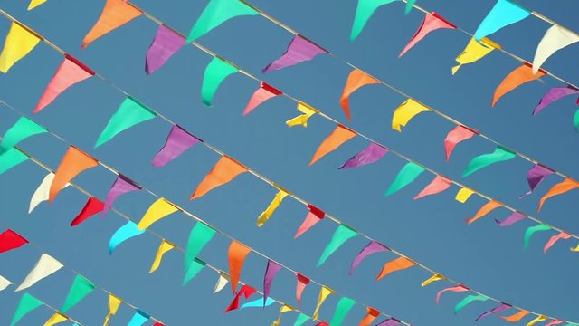 Panning shot against a clear blue sky background of colorful string pennant triangle flags used for celebrations or grand openings blowing in the wind.