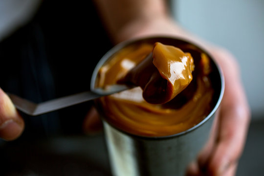 Person spooning caramel sauce from tin