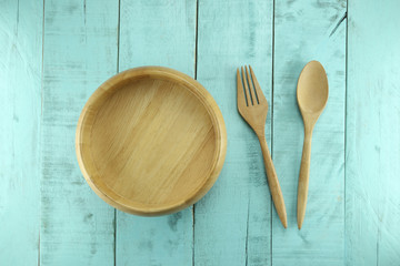 Wooden spoon and fork placed near bowl on a green wood backgroun