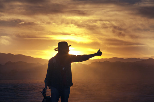 Man Hitchhiking On Road By Desert At Sunset