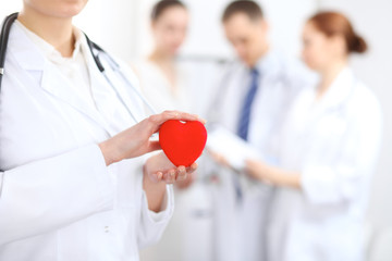 Female doctor with stethoscope holding heart.  Two doctors standing in the background