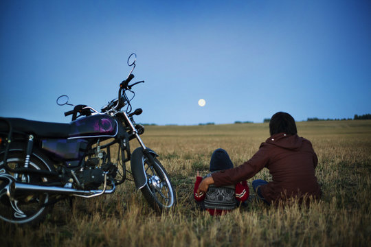 Father with son (4-5 ) sitting in field and looking at moon