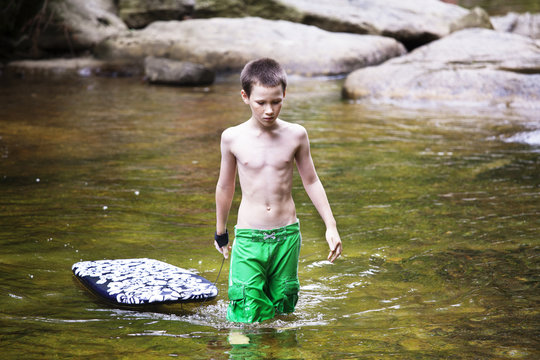 Boy (10-11) wading in river and pulling body board