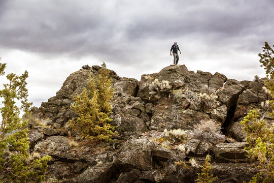 Man on top of rock formation against overcast sky,