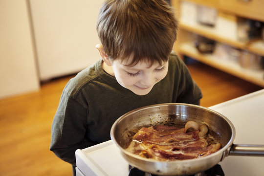 Boy looking at pan with fried bacon
