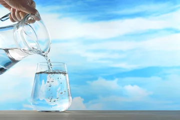 Fotobehang Water Vers en schoon drinkwater wordt gegoten uit de kruik in glas op de hemelachtergrond