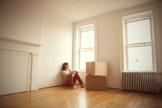 Woman sitting by window in empty apartment