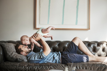 Side view of father lifting son while lying on sofa at home
