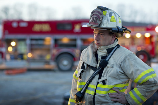 Tired firefighter looking away while standing against fire engine
